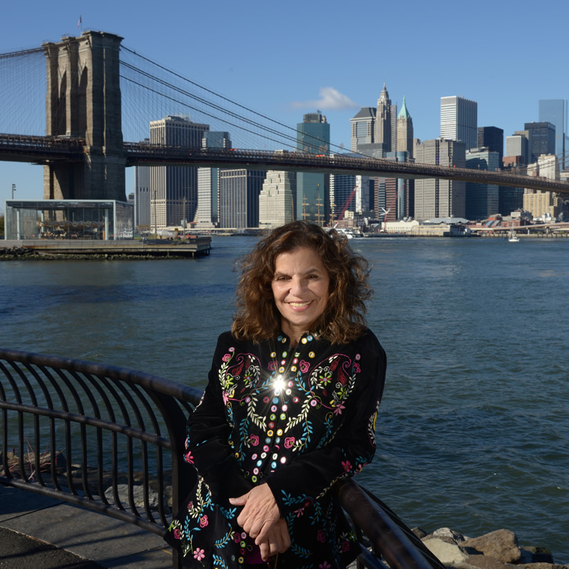 Eleanora leaning on a railing with New York bridge and skyline in the background